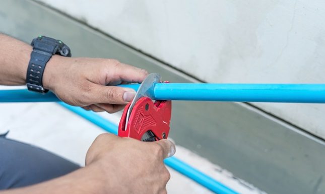 Protecting Your Property: The Importance of Timely Poly B Replacement Hands using a pipe cutter on a blue pipe, highlighting the importance of timely poly B replacement